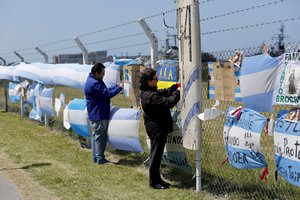 People stand in front of a fence blanketed with national flags and banners in support of the crew members of the lost submarine, outside the navel base in Mar del Plata, Argentina, Tuesday, Nov. 21, 2017.