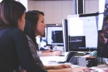 Two women working together at a computer in an office.