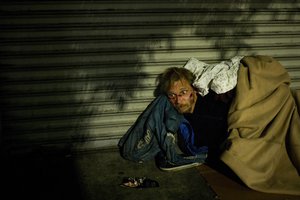 File - Bearing cuts all over his face, a homeless drug addict, who said his name is April Jane, aimlessly stares into space on a sidewalk in the Skid Row area of downtown Los Angeles, Thursday, Nov. 2, 2017.