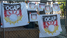 OCAP logo flags hanging from a chainlink fence