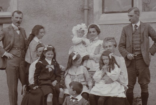 Black and white photograph of a family in front of house, c 1900