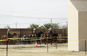 In this Oct. 19, 2017, file photo, a group of people are detained by Border Patrol agents on horseback after crossing the border illegally from Tijuana, Mexico, near prototypes for a border wall, right, being constructed in San Diego.