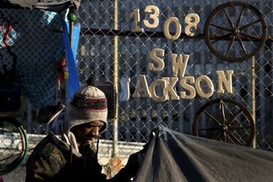 Thaddeus Bell, 50, who is homeless, sits outside his tent with the street address of his childhood home in Oklahoma hanging on a fence Monday, Dec. 4, 2017, in Los Angeles.