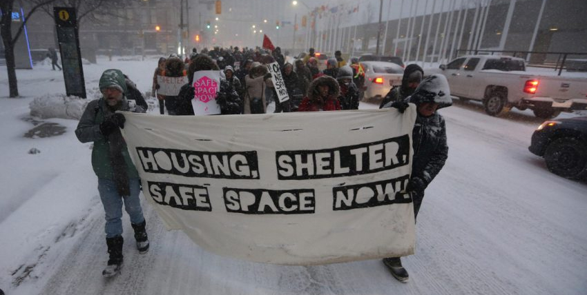 March through a blizzard to demand shelters be opened. Front banner says "Housing, Shelter, Safe Space Now!"