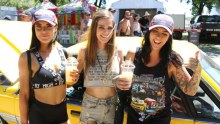 Three women stand in front of a yellow car at Summernats.