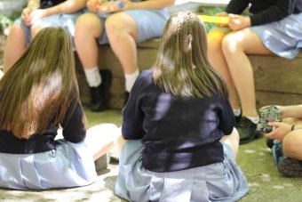 Unidentifiable teenage girls eat in a school yard.