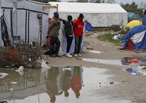 File - Migrants stand in the migrant camp known as the new Jungle of Calais, northern France, Monday, Oct. 19, 2015.