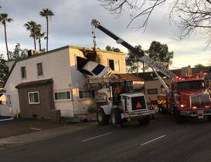 In this Sunday, Jan. 14, 2018, photo provided by Orange County Fire Authorit, a vehicle that crashed into a building hangs from a second story window in Santa Ana, Calif.