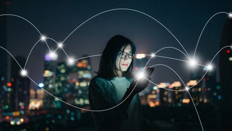 Une femme asiatique regarde son téléphone dans la pénombre avec un paysage urbain en arrière-plan. Une série de lignes courbes représentant un réseau internet parcourt la photo.