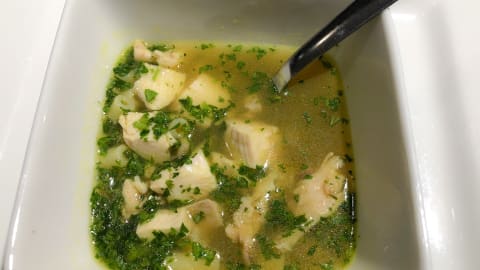 Un bouillon avec des morceaux de poulet, du persil et des nouilles