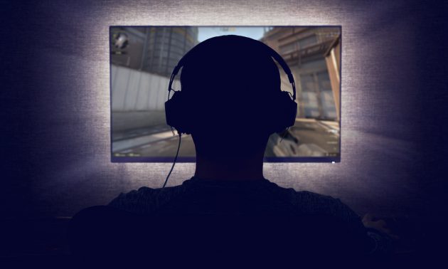 A gamer in headphones sits in front of a monitor in a darkened room. Photo: iStock/Getty Images