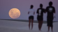 A giant moon on the horizon, with three people silhouetted next to it.