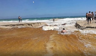 A bodyboarder slides down the stream from the river to the ocean.