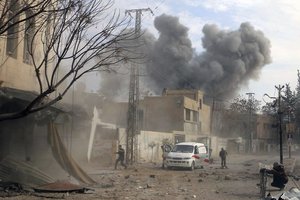 This photo provided by the Syrian Civil Defense White Helmets, which has been authenticated based on its contents and other AP reporting, shows a plume of smoke rises while civil defense workers arrive at the scene of an attack after airstrikes hit a rebel-held suburb near Damascus, Syria, Thursday, Feb. 8, 2018.