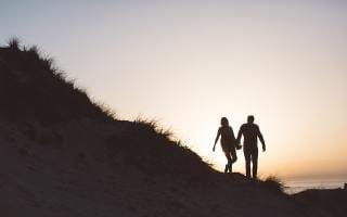 A couple walking along the coastline at dusk in Jersey