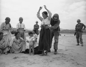 U.S.military policeman searches Korean woman refugee for possible hidden weapons on Naktong River beach in South Korea on Sept. 27, 1950 after U.S. 24th Division drive across the river west of Taegu.