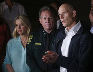 Florida Gov. Rick Scott, foreground, gestures as he speaks along with Sheriff Scott Israel, center, of Broward County, and Pam Bondi, Florida Attorney General, during a news conference near Marjory Stoneman Douglas High School in Parkland, Fla., where a former student is suspected of killing at least 17 people Wednesday, Feb. 14, 2018. The shooting at a South Florida high school sent students rushing into the streets as SWAT team members swarmed in and locked down the building. Police were warning that the shooter was still at large even as ambulances converged on the scene and emergency workers appeared to be treating those possibly wounded. (AP Photo/Wilfredo Lee)