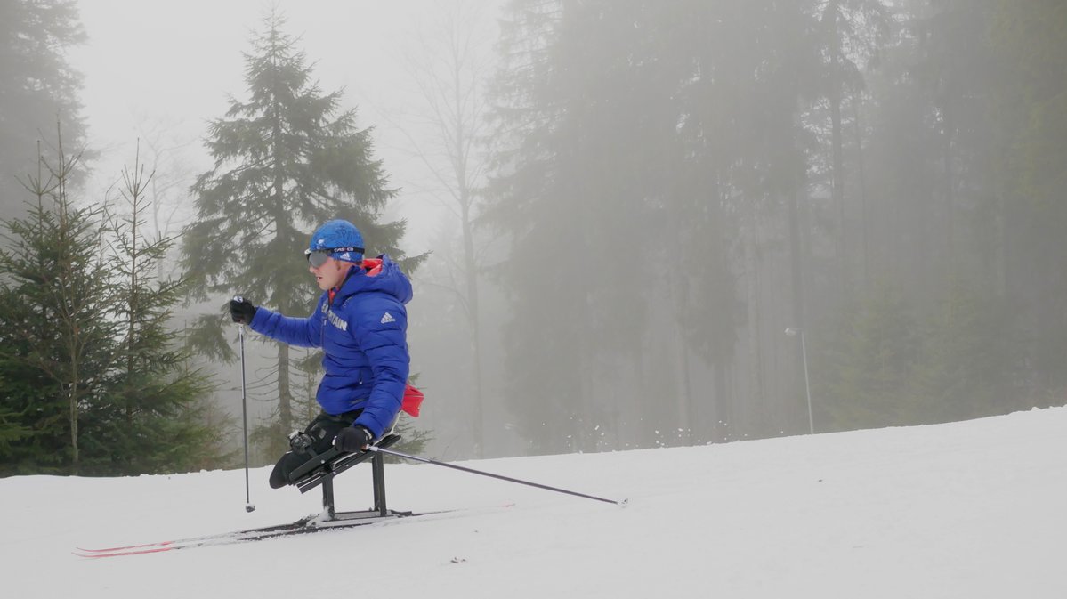 Scott Meenagh sit-skis in a snowy woodland