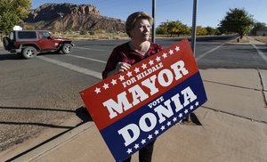 In this Thursday, Oct. 26, 2017 photo, Donia Jessop holds her mayoral campaign sign outside her store in Colorado City, Ariz. Campaign signs are unusual in a town where elections have long been quietly decided behind the scenes, with hand-picked men from the Fundamentalist Church of Jesus Christ of Latter-Day Saints running unopposed. (AP Photo/Rick Bowmer)