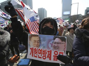 In this March 1, 2018, photo, a conservative activist with a card showing a portrait of South Korean President Moon Jae-in and North Korean leader Kim Jong Un, right, attends a ceremony to celebrate the March First Independence Movement Day, the anniversary of the 1919 uprising against Japanese colonial rule, in Seoul, South Korea.