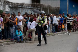 Flanked by police in riot gear, people line up outside of a supermarket to buy regulated food in Caracas, Venezuela, Wednesday, June 1, 2016.