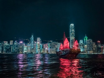 Taken on Victoria Harbour in Hong Kong, the old and the new glow with life. A red sailed Junk carries a load of tourists ...