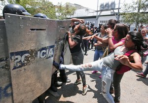 A woman kicks at a riot police shield as relatives of prisoners wait to hear news about their family members imprisoned at a police station where a riot broke out, in Valencia, Venezuela, Wednesday, March 28, 2018.