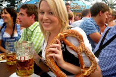 C8WJN1 Young woman enjoying pretzel and stein of beer at Oktoberfest