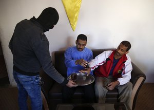 A Kurdish security officer offers tea to Alexanda Amon Kotey, center, and El Shafee Elsheikh, right, Alexanda Amon Kotey, left, and El Shafee Elsheikh, who were allegedly among four British jihadis who made up a brutal Islamic State cell dubbed "The Beatles," during an interview with The Associated Press at a security center in Kobani, Syria, Friday, March 30, 2018.