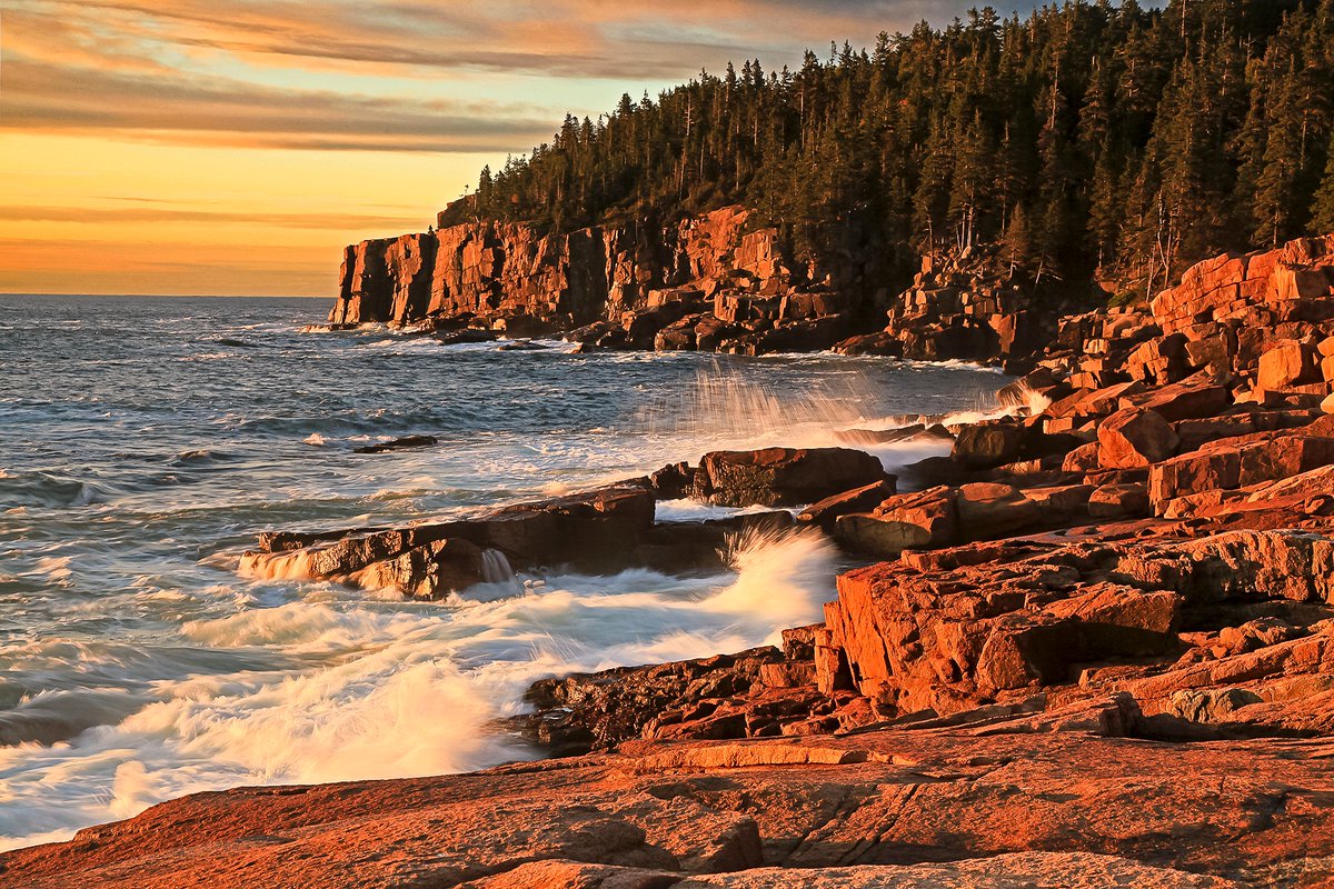 Ocean waves crash against a rocky coastline of boulders and stone cliffs.