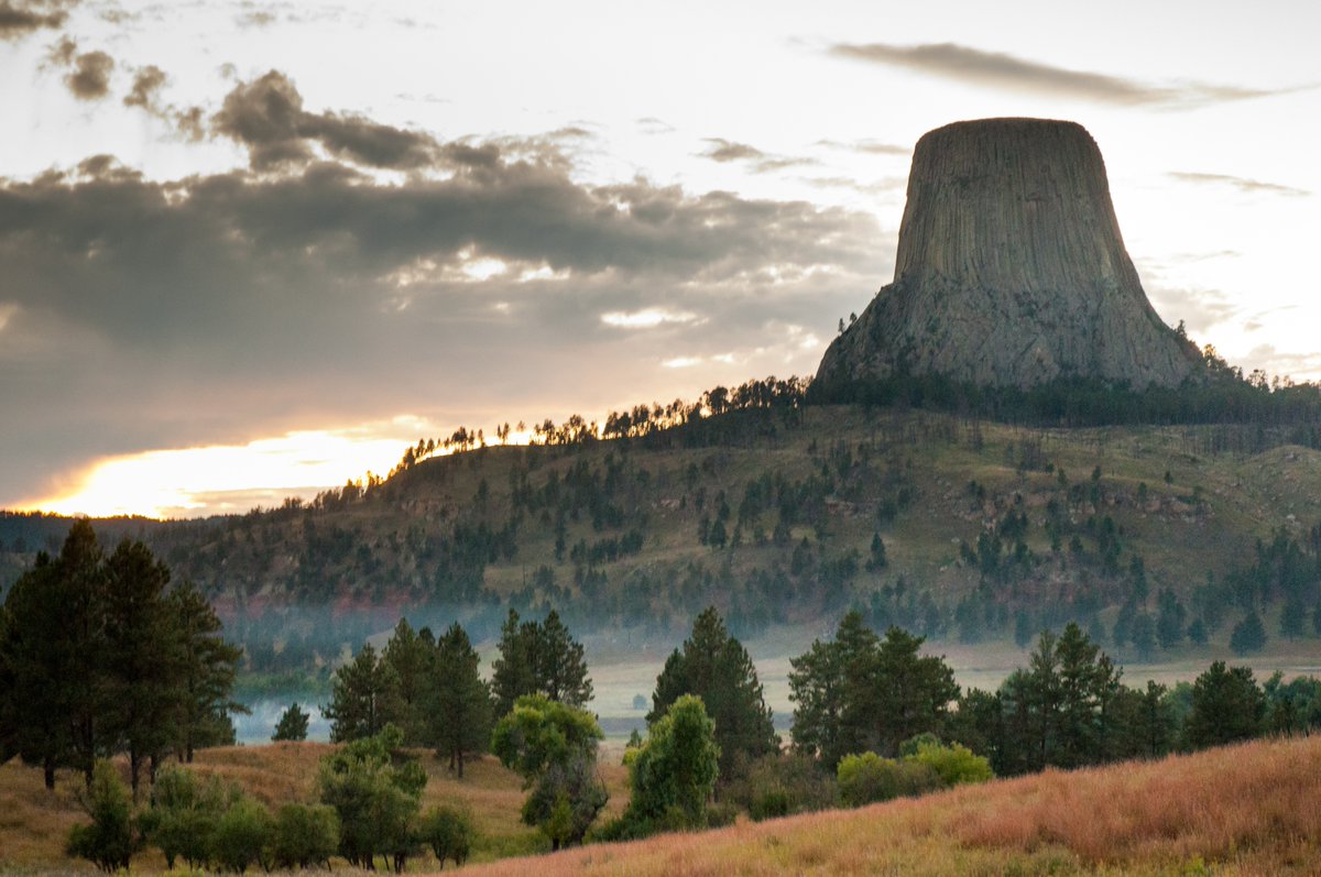 A tall cylinder shaped mountain stands on a hill dotted with trees.