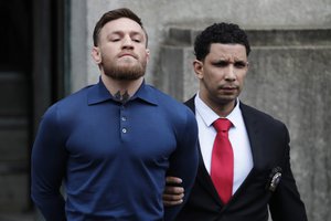 Ultimate fighting star Conor McGregor, left, is led by an official to an unmarked vehicle while leaving the 78th Precinct of the New York Police Department, Friday, April 6, 2018, in the Brooklyn borough of New York.