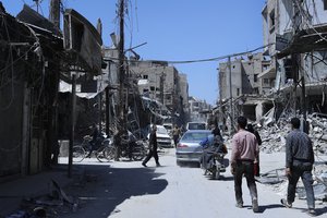 People walk among damaged buildings in the town of Douma, the site of a suspected chemical weapons attack, near Damascus, Syria, Monday, April 16, 2018.