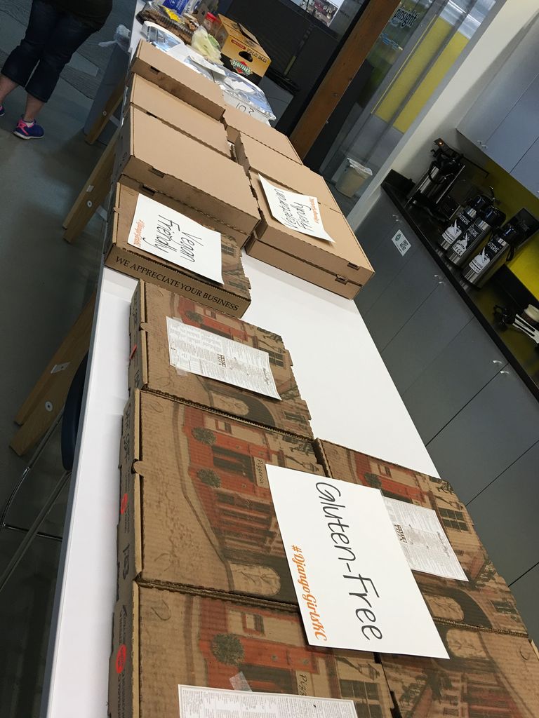 Pizza boxes are laid out in a row on a white table. Some of them are labeled "Gluten-Free", "Vegan Friendly" or "Vegetarian Friendly"