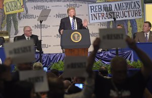 Protesters hold up signs as President Donald Trump speaks at the 2017 North America's Building Trades Unions National Legislative Conference in Washington, Tuesday, April 4, 2017.