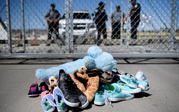 Security personal stand before shoes and toys left at a Port of Entry where minors crossing the border have been housed after being separated from adults, June 21, 2018. (Photo by Brendan Smialowski / AFP)