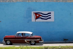 A man drives a car beside a wall decorated with a national flag in Havana, Cuba, Sunday, June 3, 2018.