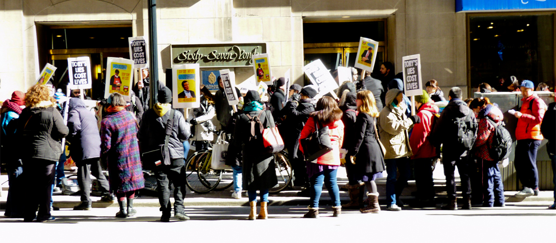 Protesters outside of CD Howe meeting where John Tory is speaking, holding "Tory's Lies Cost Lives" and other placards agains't Tory's cuts to shelters