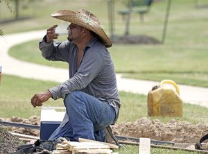 Construction worker Ramiro Montez drinks water while kneeling in the shade as he takes a break from working outside in the heat Monday, July 23, 2018, in Houston.