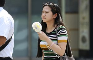 A woman holds a portable fan at a business district in Tokyo, Monday, July 23, 2018.