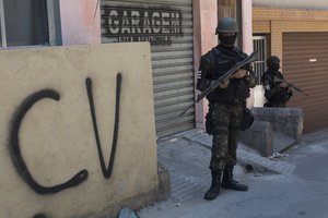 A soldier stands guard next to a wall tagged with the acronym "CV" identifying the criminal organization "Comando Vermelho" or Red Command, during an operation at the Rocinha slum, in Rio de Janeiro, Brazil, Tuesday, Oct. 10, 2017. More than 1,000 Brazilian police and soldiers are searching Rio de Janeiro's largest slum for weapons and ammunition amid a crackdown on drug gangs