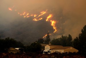 In this Aug. 9, 2018, file photo a wildfire in the Cleveland National Forest at a hillside near homes in Lake Elsinore, Calif. California homeowners may find themselves facing insurance issues even if they were not directly hit by this year’s blazes.