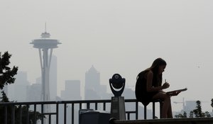 A girl works on a drawing next to an unused viewing scope as a smoky haze obscures the Space Needle and downtown Seattle behind, Tuesday, Aug. 14, 2018