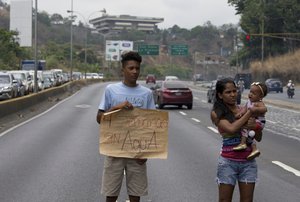 A demonstrator holds up a poster that reads in Spanish "Four weeks without water" during a protest demanding the service suspended one month ago, in Caracas, Venezuela, Friday, April 27, 2018.