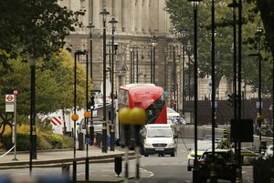 A forensics officer works near the scene near of a car that crashed into security barriers outside the Houses of Parliament to the right of a bus in London, Tuesday, Aug. 14, 2018.