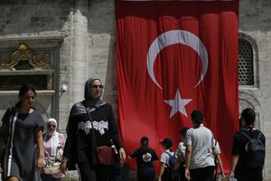 People walk past a Turkish flag on a mosque compound in Istanbul, Wednesday, Aug. 15, 2018.