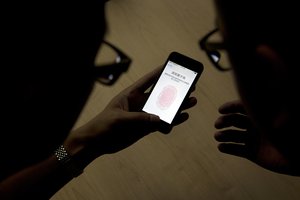 In this Sept. 11, 2013, file photo, an Apple employee, right, instructs a journalist on the use of the fingerprint scanner technology built into the company's iPhone 5S during a media event in Beijing.