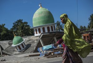 In this Saturday, Aug. 11, 2018, photo, a Muslim woman walks past a mosque collapsed during Sunday's earthquake in Gangga, Lombok Island, Indonesia.