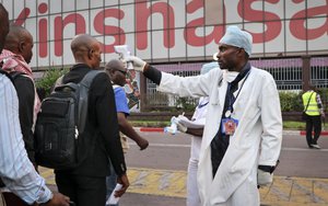 File - In this photo taken Saturday, June 2, 2018, a health worker checks people's temperatures as they disembark a plane at the airport in Kinshasa, Congo.