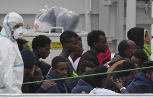 Migrants stand aboard the Italian Coast Guard ship Diciotti, moored at the Catania harbor, Tuesday, Aug. 21, 2018.